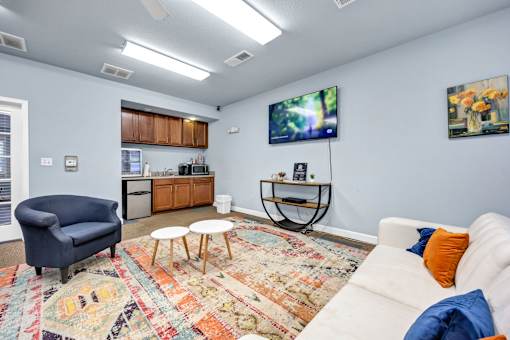 A living room with a white couch, a blue armchair, and a rug with a pattern.