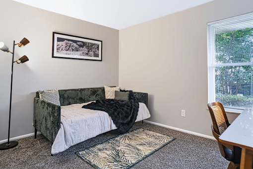 A bedroom with a bed, chair, and a picture on the wall.