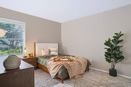 A bedroom with a bed, a potted plant, and a table with a vase on it.