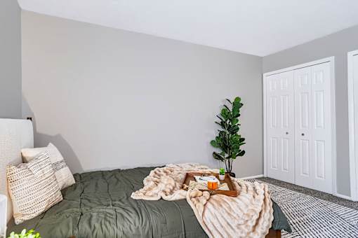 A cozy bedroom with a bed covered in a green comforter and a tray with a book and a plant on it.