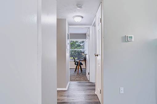 A hallway with a door on the right and a window with a view of trees outside.