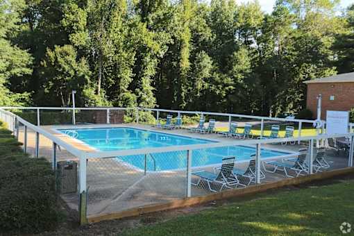 A pool surrounded by trees and chairs.