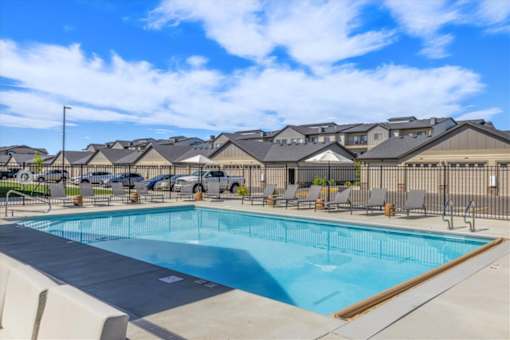 A swimming pool surrounded by lounge chairs and umbrellas in front of a row of houses.