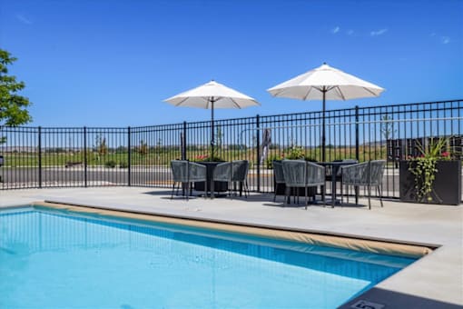 A pool with chairs and umbrellas is surrounded by a black fence.