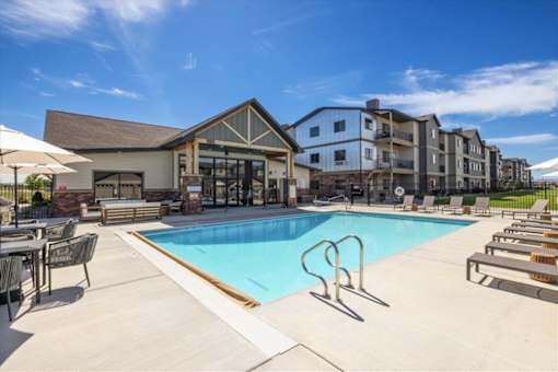 A large swimming pool in front of a building with lounge chairs around it.