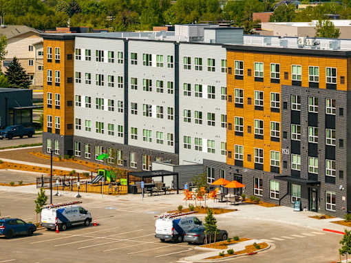 A parking lot with a few cars and a building in the background at The Beaumont Apartments, Montana, 59715
