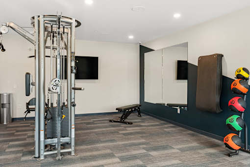 A gym room with a weight machine, a bench, and a mirror at The Beaumont Apartments, Bozeman