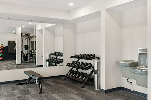 A gym room with a bench, weights, and a mirror at The Beaumont Apartments, Bozeman