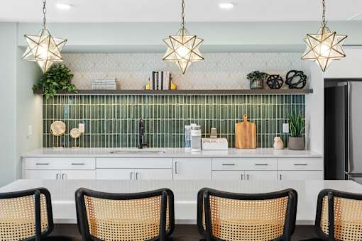 A kitchen with white cabinets and a green backsplash with three hanging lights at The Beaumont Apartments, MT 59715