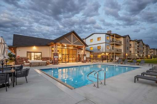 A swimming pool is surrounded by lounge chairs and umbrellas outside a building.