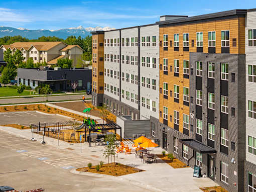 A modern apartment complex with a parking lot in front at The Beaumont Apartments, Montana, 59715