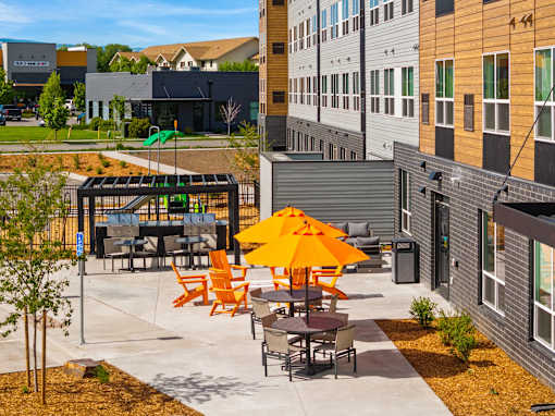 A patio with orange chairs and tables is surrounded by buildings at The Beaumont Apartments, Bozeman, 59715