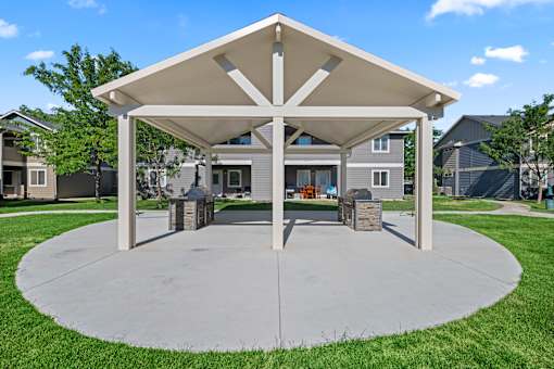 A pavilion with a white roof and pillars is surrounded by a grassy area.