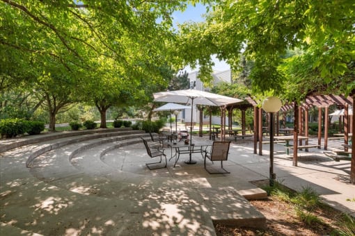 a patio with tables and umbrellas in a park with trees