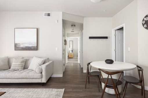 a small table and chairs in a living room with a couch and a hallway in the background at The Alloy at Geneva, Vineyard, UT, 84058