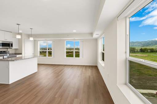 A modern kitchen with wooden floors and a large window overlooking a green landscape at The Beaumont Apartments, Bozeman