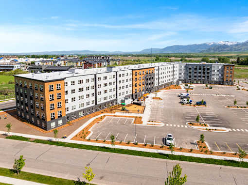 A large multi-story building with a parking lot in front at The Beaumont Apartments, Bozeman