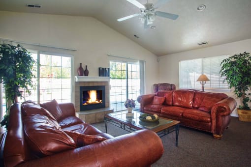 View of resident sitting room with two brown leather look couches facing one another with a stone-framed fireplace on the wall between at Country Oaks Apartments in UT 80415