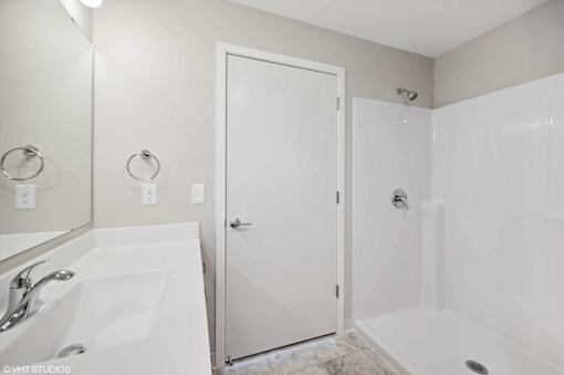A white bathroom with a sink, mirror, and shower.
