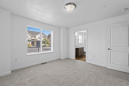 A room with a carpeted floor and a large window showing a house outside.