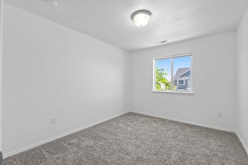 A room with a carpeted floor and a window showing a house outside.