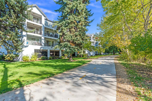 a sidewalk in front of an apartment building with trees and grass at River Walk Apartments, Boise, ID