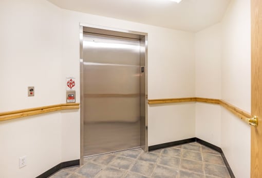 a stainless steel elevator in a white walled room with a wooden railing