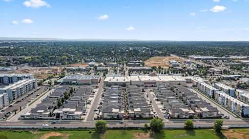 A large, open parking lot is surrounded by apartment buildings and a distant cityscape. at Verraso Village Apartments, Meridian 83646