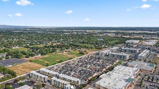 A large parking lot is surrounded by buildings and greenery. at Verraso Village Apartments, Idaho, 83646