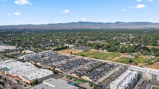 A large parking lot is surrounded by buildings and a green field. at Verraso Village Apartments, Meridian, ID