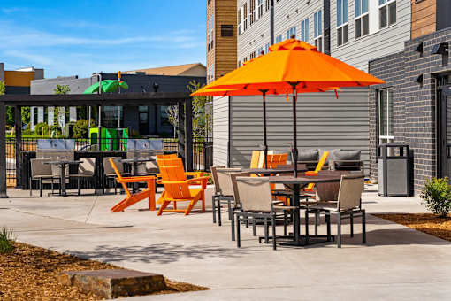 A patio with orange chairs and an orange umbrella at The Beaumont Apartments, Montana