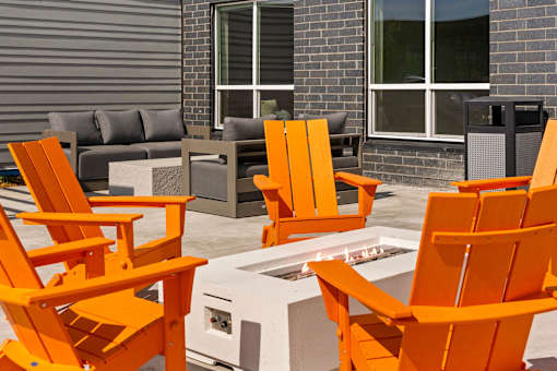A set of orange chairs are arranged around a fire pit at The Beaumont Apartments, MT 59715