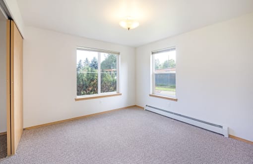 an empty living room with two windows and a carpet