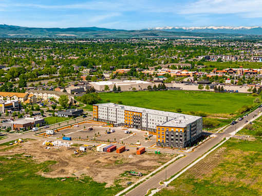A large building with a grey and yellow exterior is surrounded by a parking lot and construction equipment at The Beaumont Apartments, Montana
