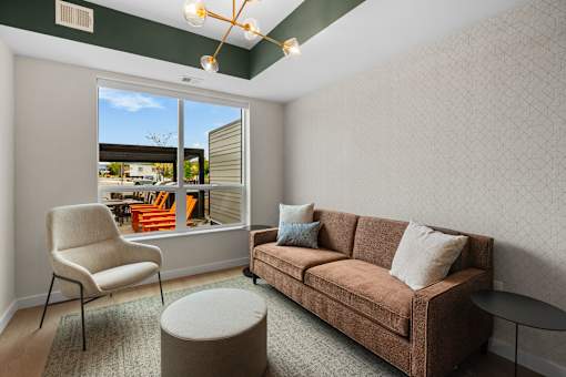 A living room with a brown couch, a chair, and a small ottoman at The Beaumont Apartments, Bozeman, MT
