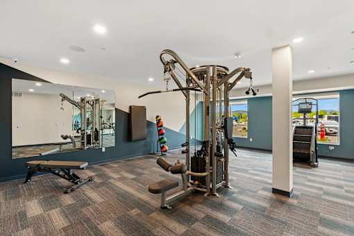 A gym with a variety of equipment including a treadmill, a bench, and a mirror at The Beaumont Apartments, Bozeman, Montana 59715
