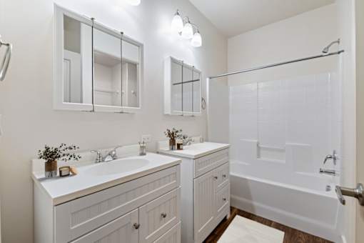 A white bathroom with a double sink and a walk-in shower. at Verraso Village Apartments, Idaho, 83646