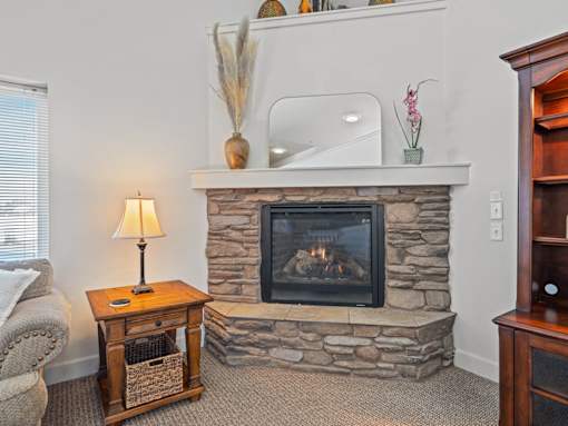 A cozy living room with a stone fireplace and a side table with a lamp.