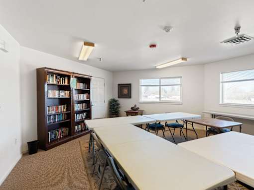 A room with a long table, chairs, and a bookcase filled with books.