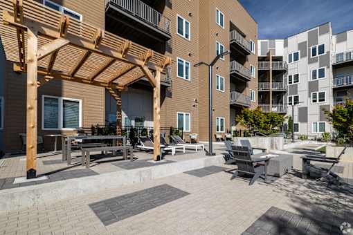 A patio area with a wooden pergola and seating area in front of apartment buildings.