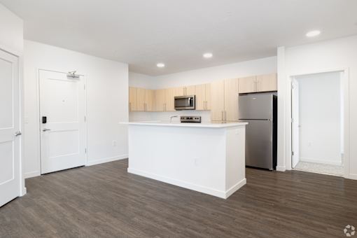 A kitchen with white cabinets and a white island with a refrigerator on the right side.