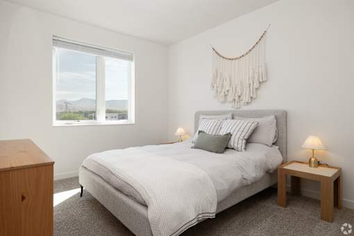 A bedroom with a large bed, a nightstand, and a window with a view of the mountains.