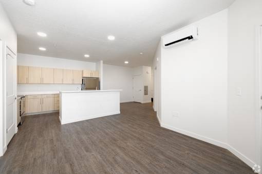 A spacious room with wooden flooring and a kitchen area with white cabinets.