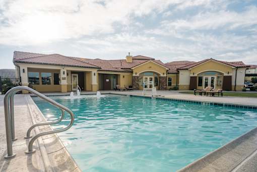 A swimming pool in front of a building with a metal railing on the left side.