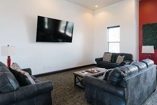 A black leather couch sits in a living room with a flat screen TV mounted on the wall.