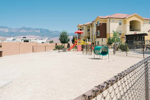 A playground with a slide and swings in front of a building with a mountain in the background.