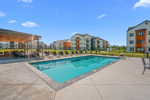 A swimming pool surrounded by lounge chairs and view of outdoor lounge area and apartment buildings at Silverbrook Apartments, Kalispell