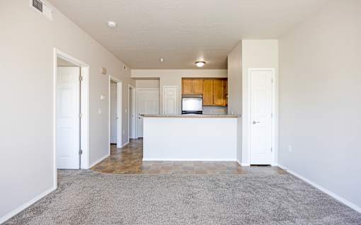 A spacious living room with a kitchen area in the background.