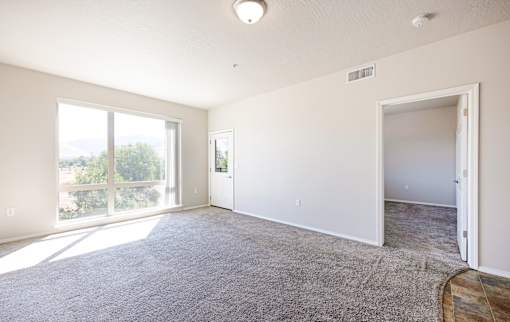 A spacious room with a carpeted floor and sliding glass doors leading to a balcony.