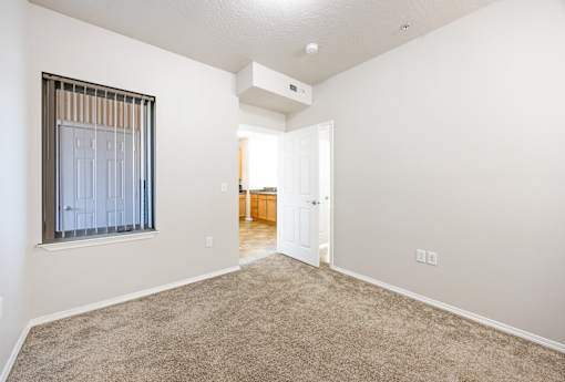 A room with a carpeted floor and a window with blinds.